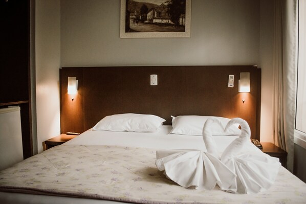 A hotel room with a neatly made bed, two bedside lamps, a framed picture on the wall, and a window with curtains. - Hotel Colina São Francisco (Gramado)