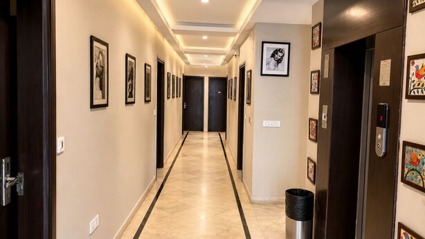 A hotel hallway with framed artwork on the walls, a trash bin, and an elevator. - The Orion Express (Jaipur)