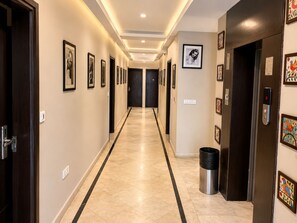 Un couloir d’hôtel avec des œuvres d’art encadrées accrochées aux murs, une poubelle et un ascenseur.