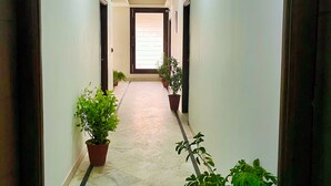 A hallway with potted plants, a tiled floor, and doors on both sides. - The Orion Express (Jaipur)