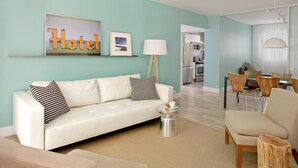 A modern hotel room with a teal accent wall, a white sofa, a dining area with a table and chairs, and a kitchen visible through an open doorway. - 1818 Meridian House Apartments and Suites by Eskape Collection (Miami Beach)