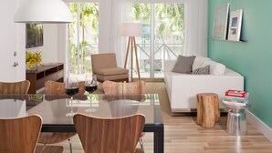 A modern living room with a glass dining table, wooden chairs, a white sofa, and a view of palm trees through large windows. - 1818 Meridian House Apartments and Suites by Eskape Collection (Miami Beach)
