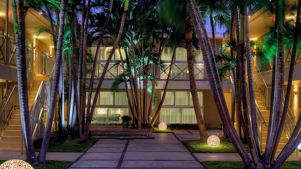 A hotel entrance with a central pathway flanked by palm trees, a staircase, and a seating area with a lamp. - 1818 Meridian House Apartments and Suites by Eskape Collection (Miami Beach)