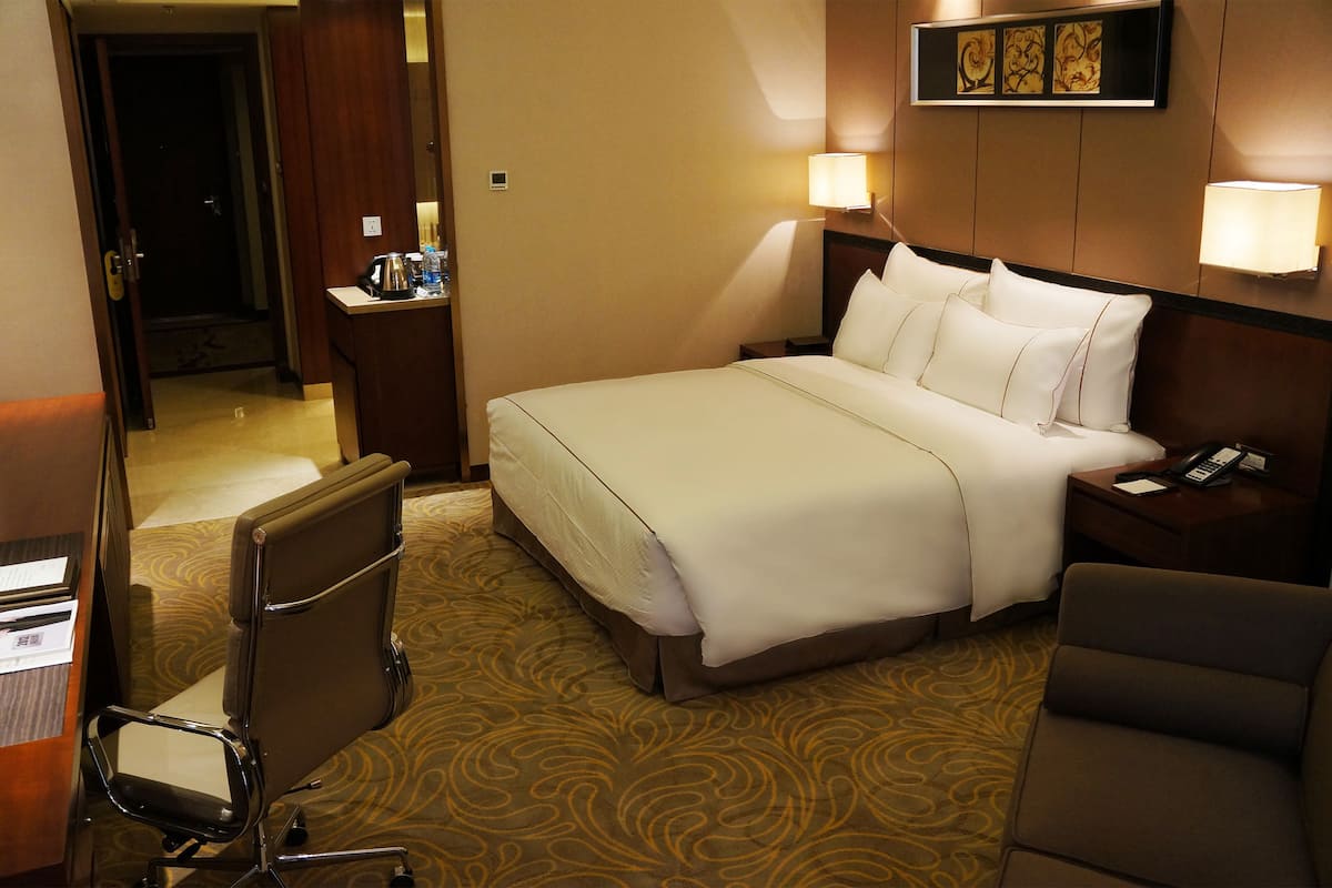 A hotel room with a bed, two bedside lamps, a desk with a telephone, and a chair.