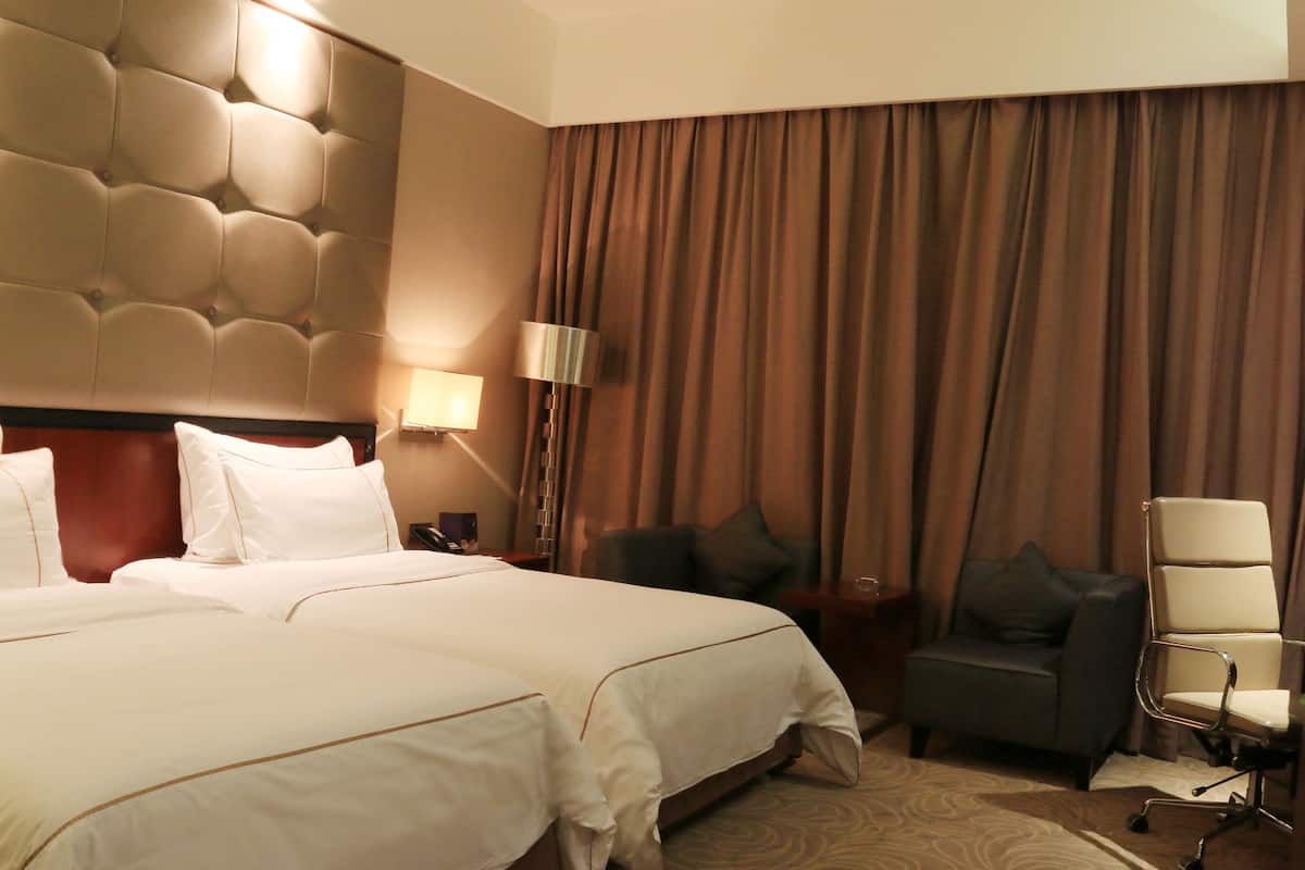 A hotel room with a large bed, a dark armchair, a desk with a lamp, and a view of a curtain.