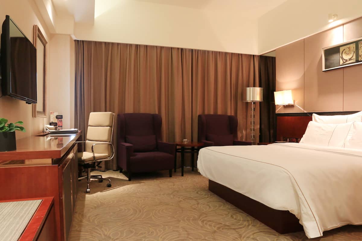 A hotel room with a large bed, two armchairs, a desk with a computer, a TV, and a lamp.