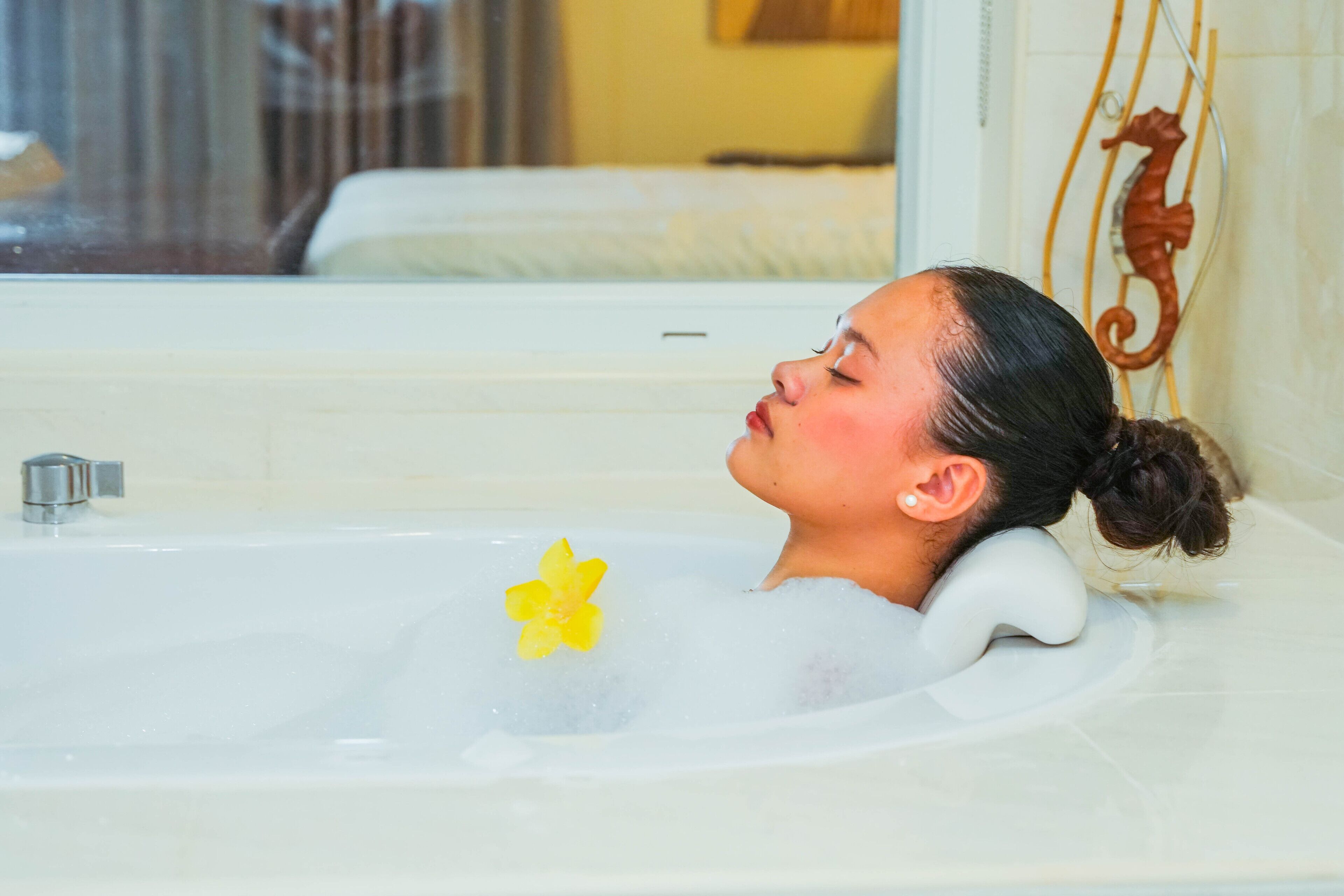 Una vasca da bagno con un fiore, una decorazione a forma di cavalluccio marino e una finestra sullo sfondo.