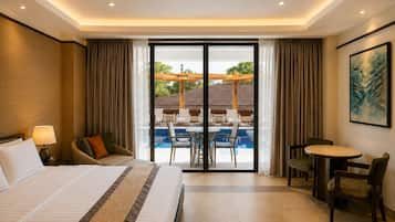 A hotel room with a bed, a desk, a chair, a dining table, and a view of an outdoor pool area.