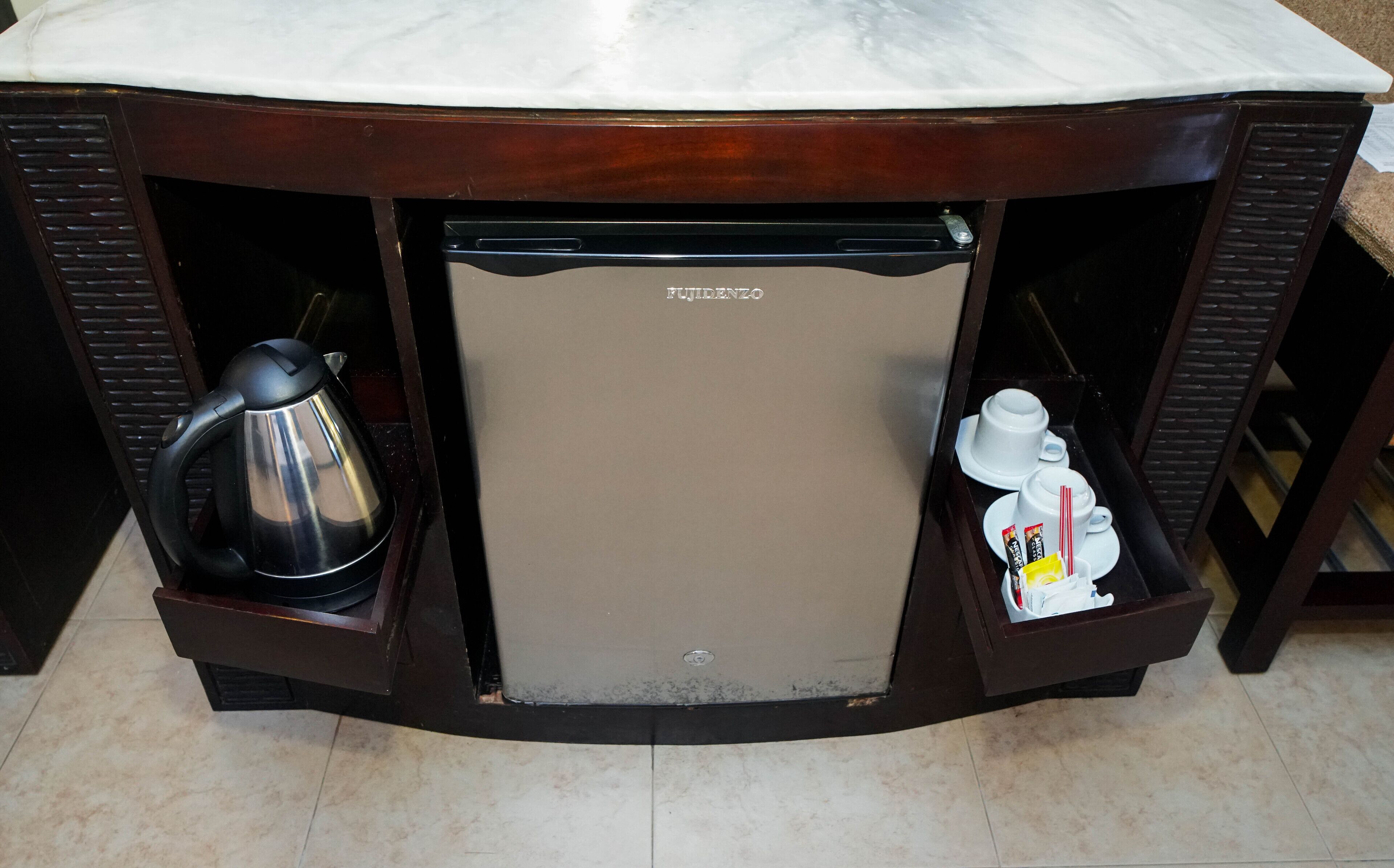 A compact refrigerator with a marble top, a kettle, and a small tea set.