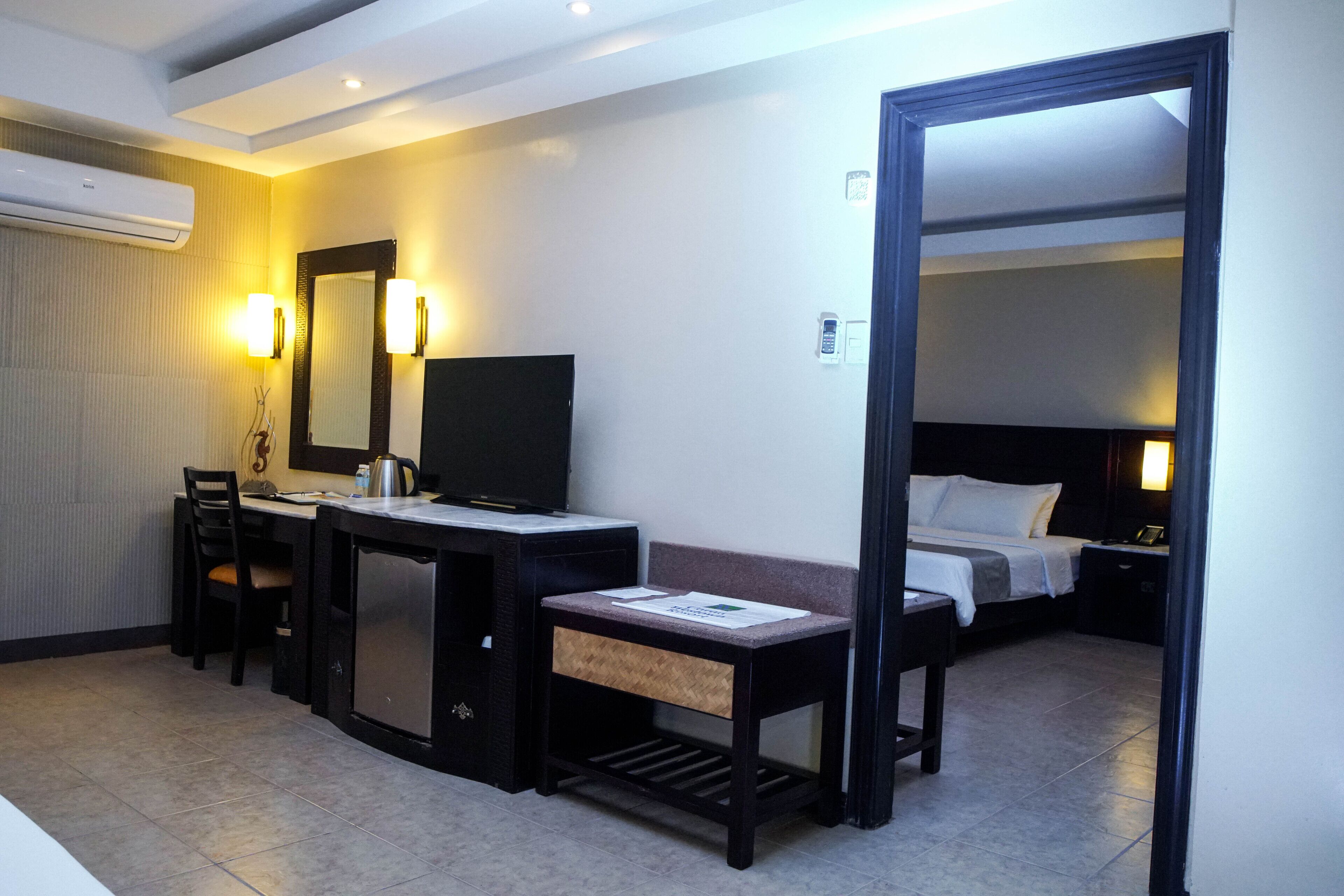 Een hotelkamer met een bureau, stoel, televisie, bed, nachtkastje en een spiegel.