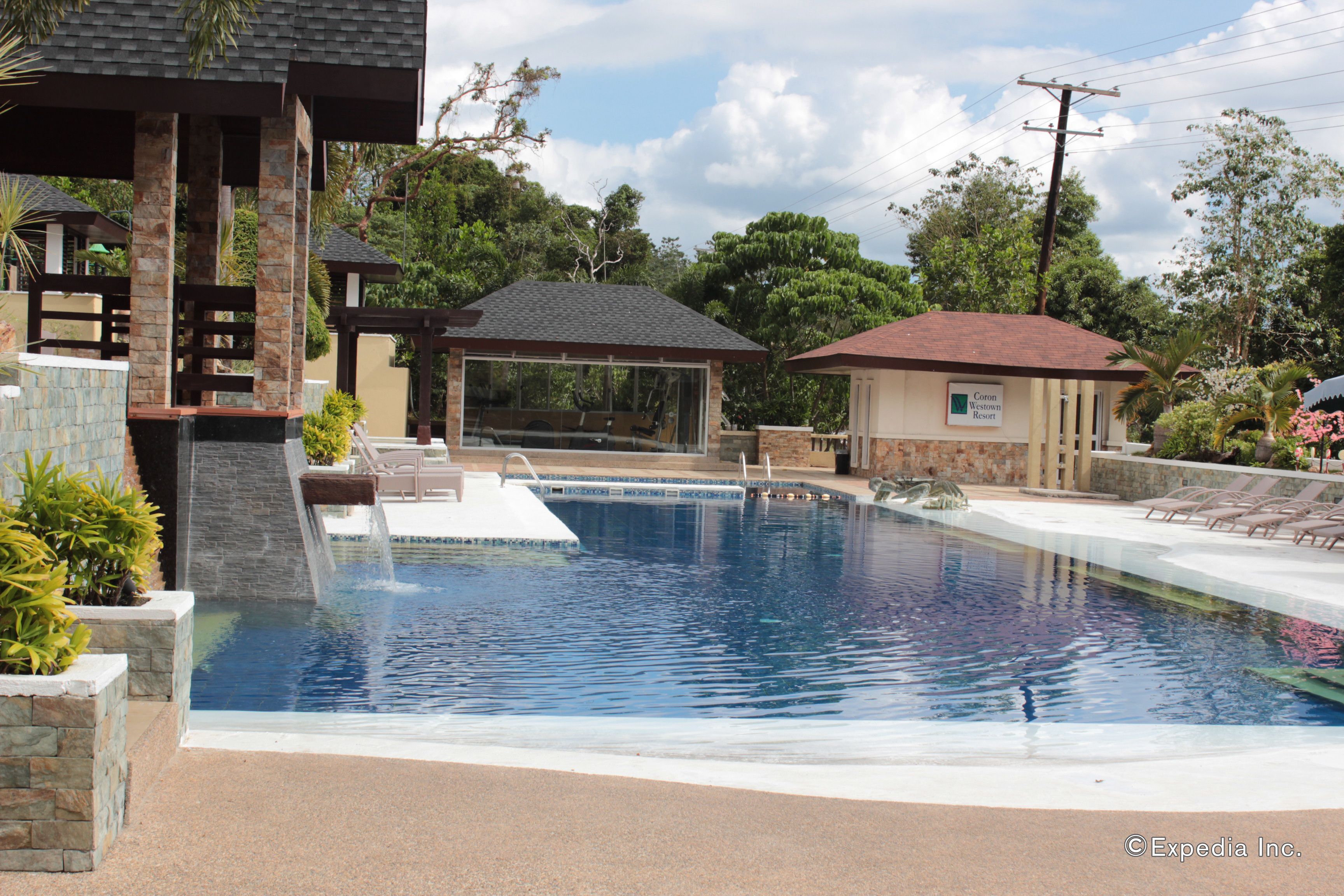 A swimming pool with a waterfall feature, lounge chairs, and a gazebo.