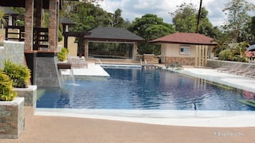 A swimming pool with a waterfall feature, lounge chairs, and a gazebo.