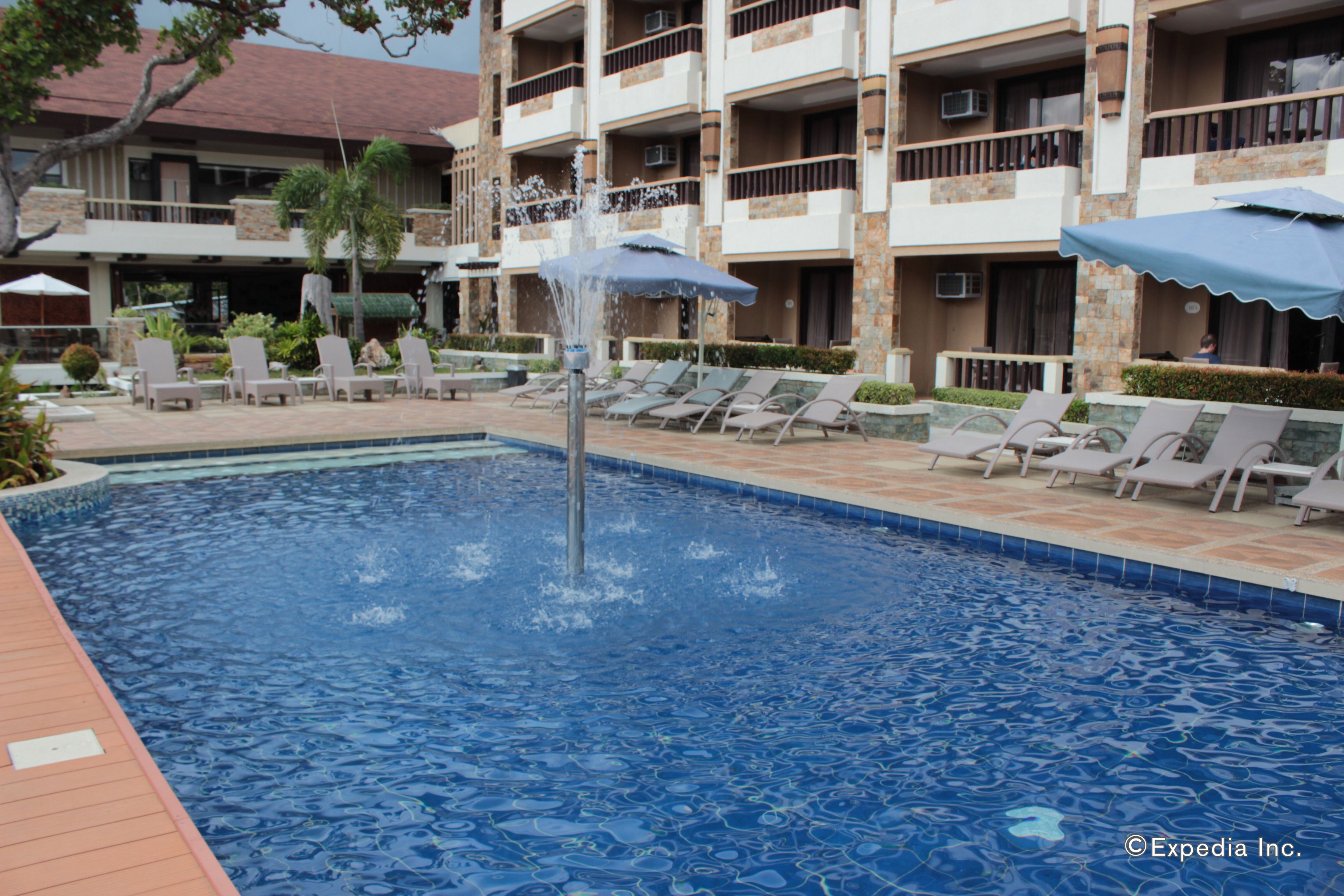 Une piscine entourée d’un bâtiment doté de balcons, avec des chaises longues et des parasols à proximité.