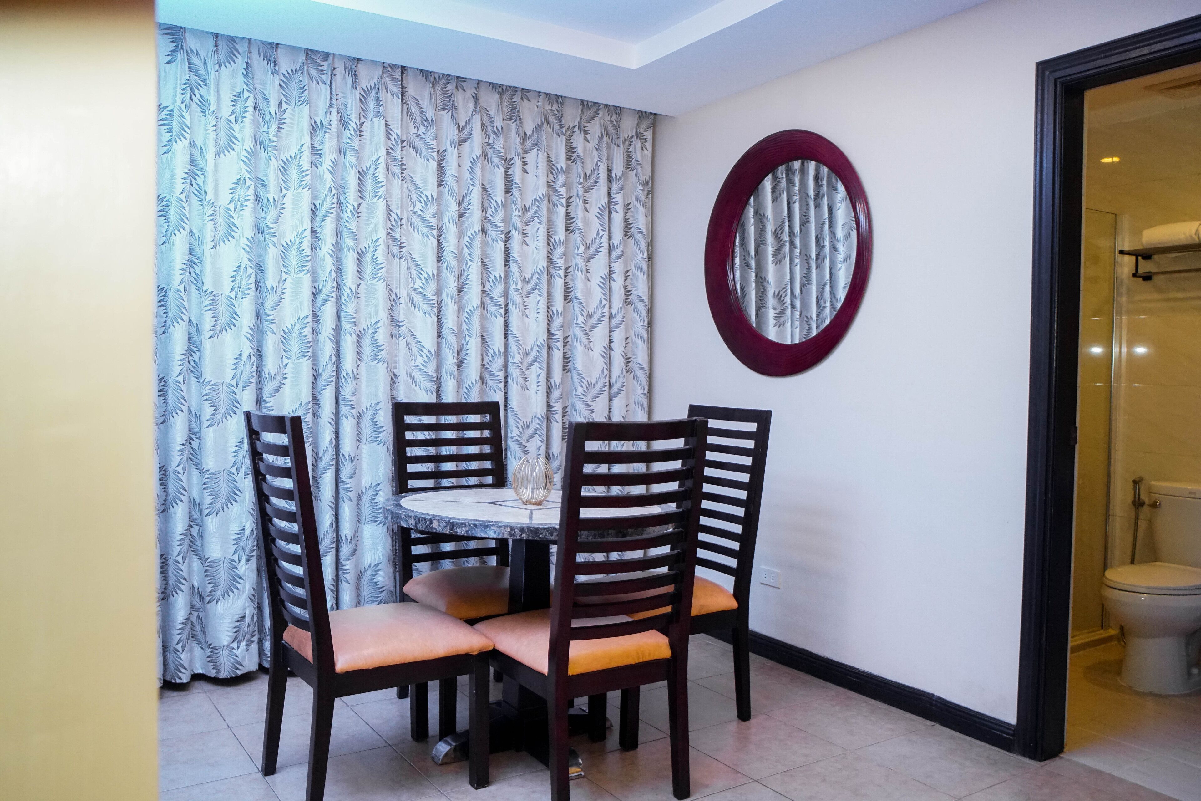 A dining area with a round table and four chairs, a patterned curtain, and a mirror on the wall.