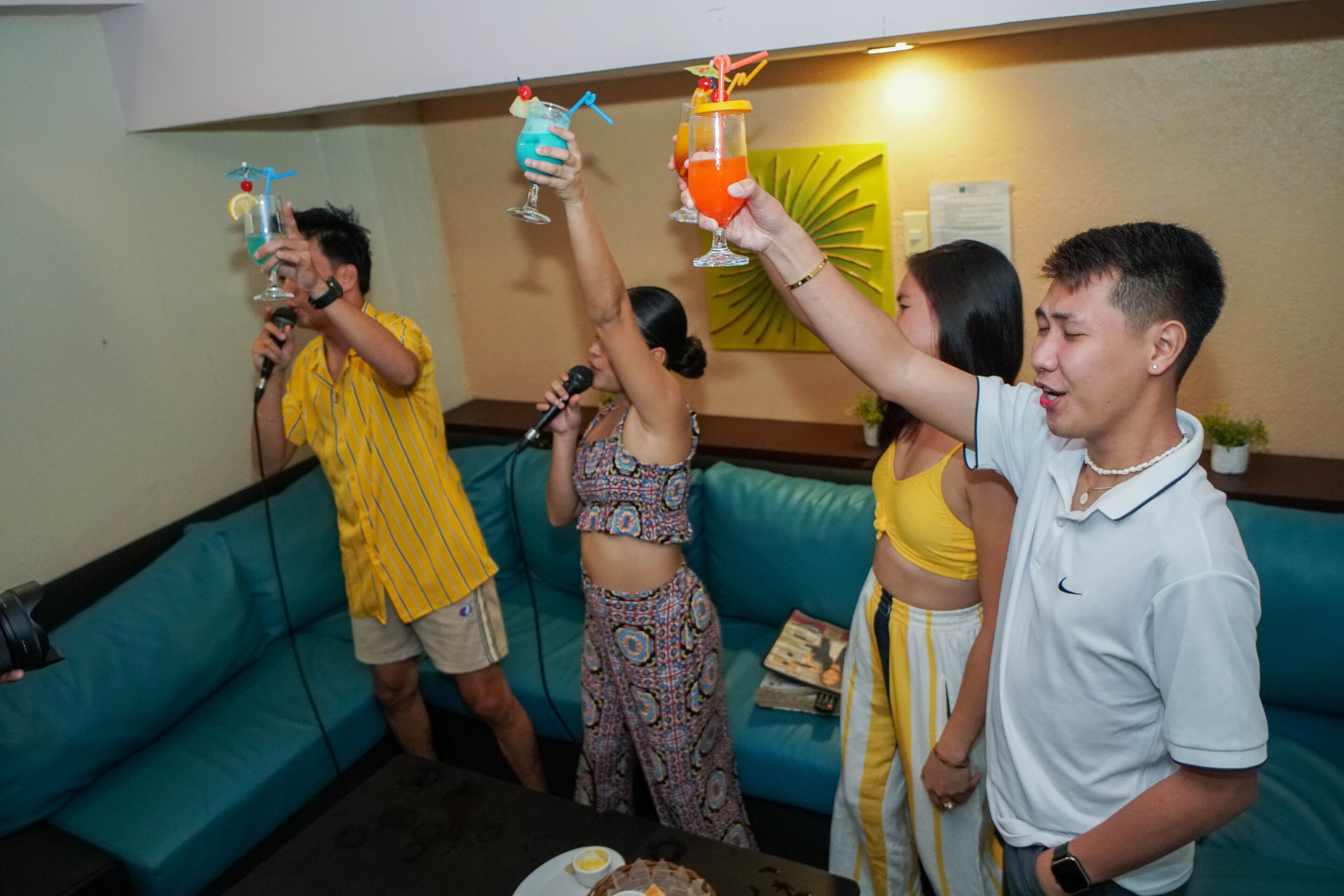 A group of people holding drinks in a room with a blue couch and a table with a cake.