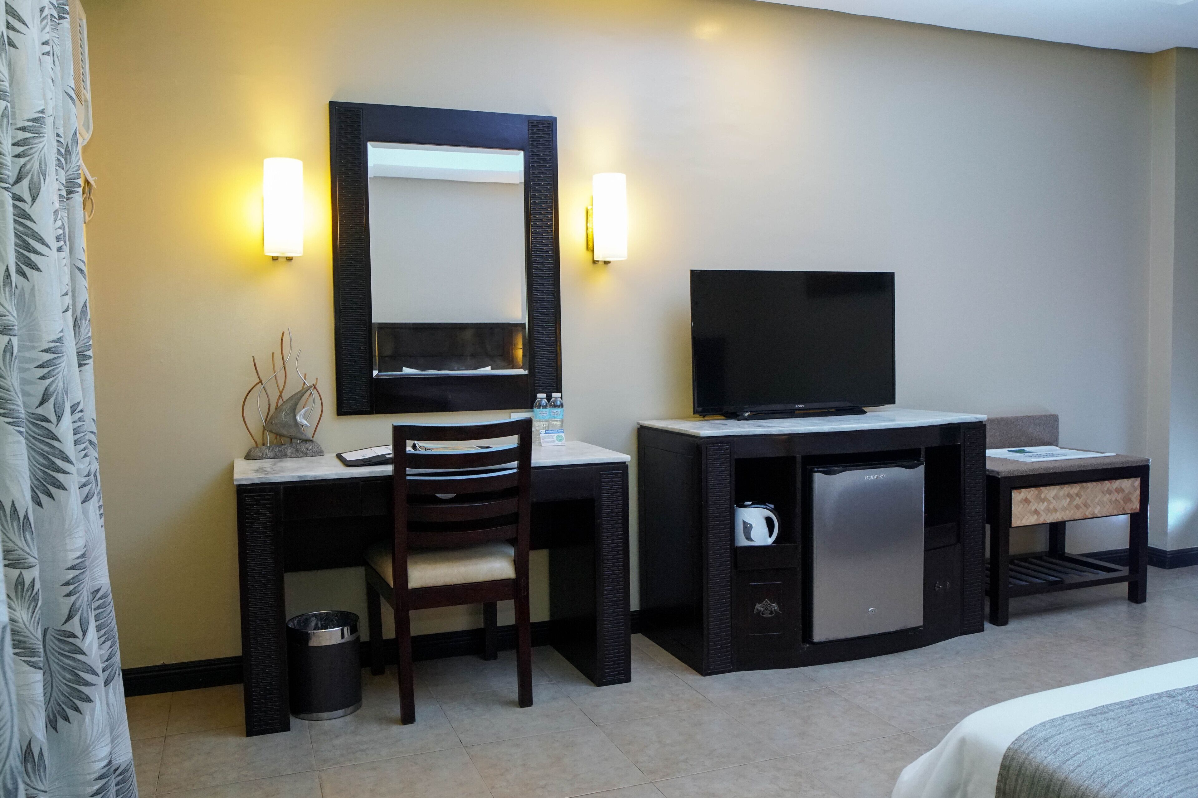 A hotel room with a desk, chair, television, minibar, and a bed.