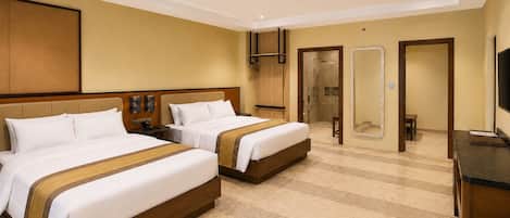 A hotel room with two beds, a desk, a mirror, and a shower area.