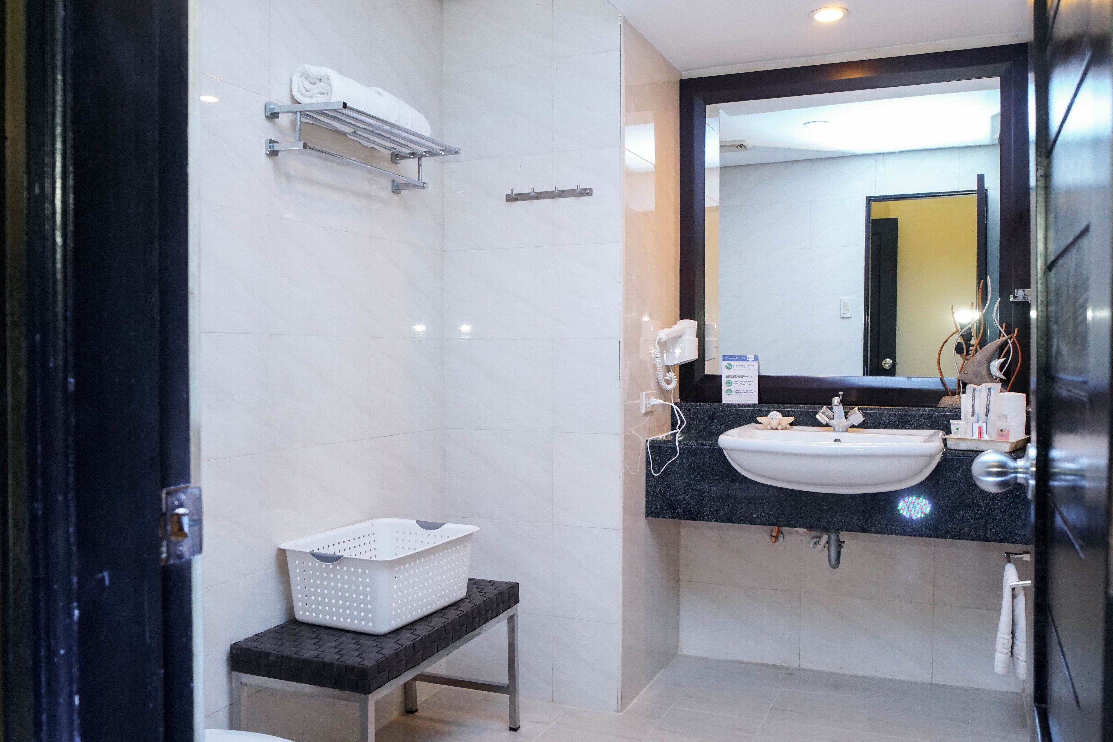 A modern bathroom with a black countertop, white sink, and a large mirror. There is a white towel rack and a small table with a white basket.