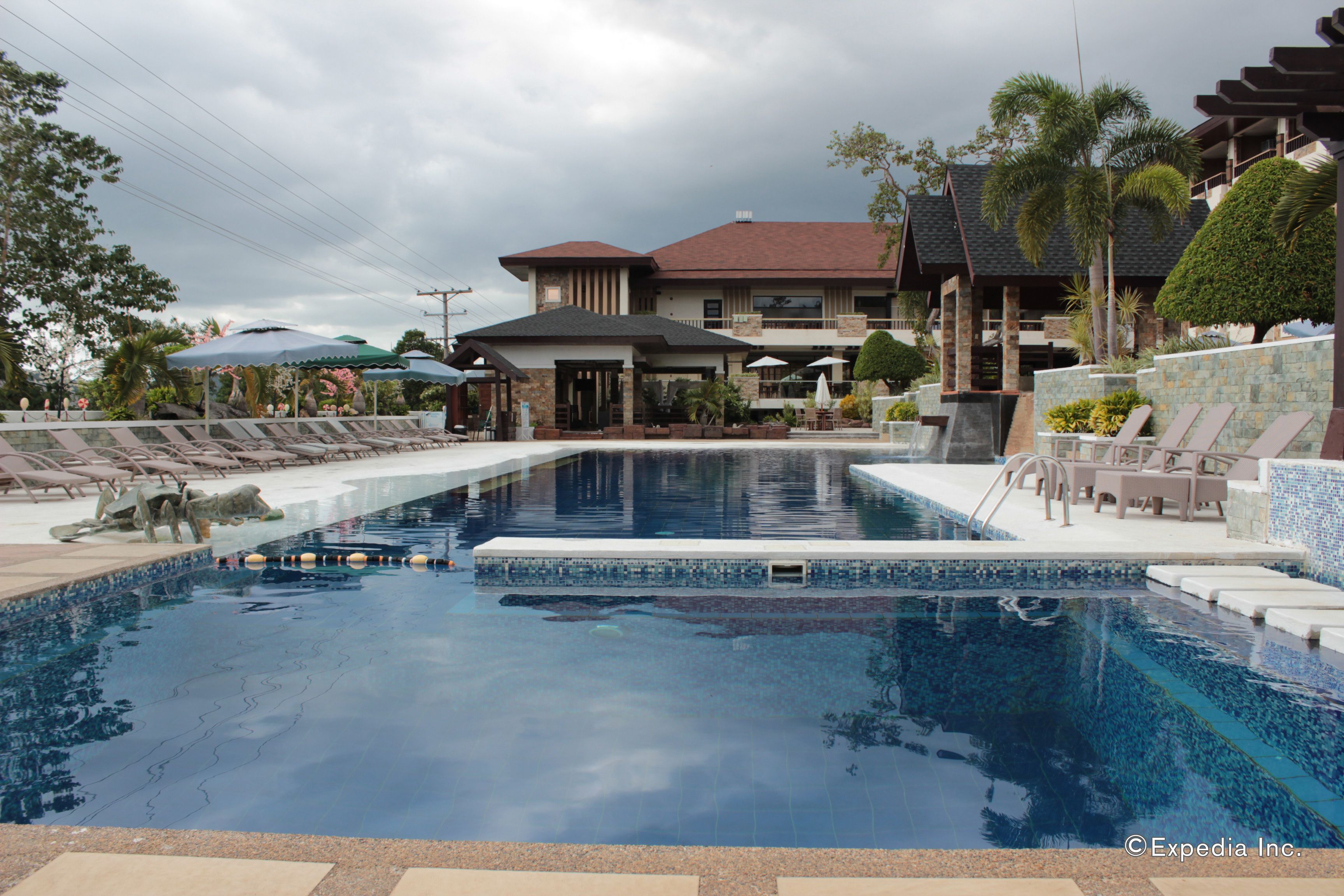 A swimming pool with lounge chairs and umbrellas, surrounded by a building with a red roof and stone walls.
