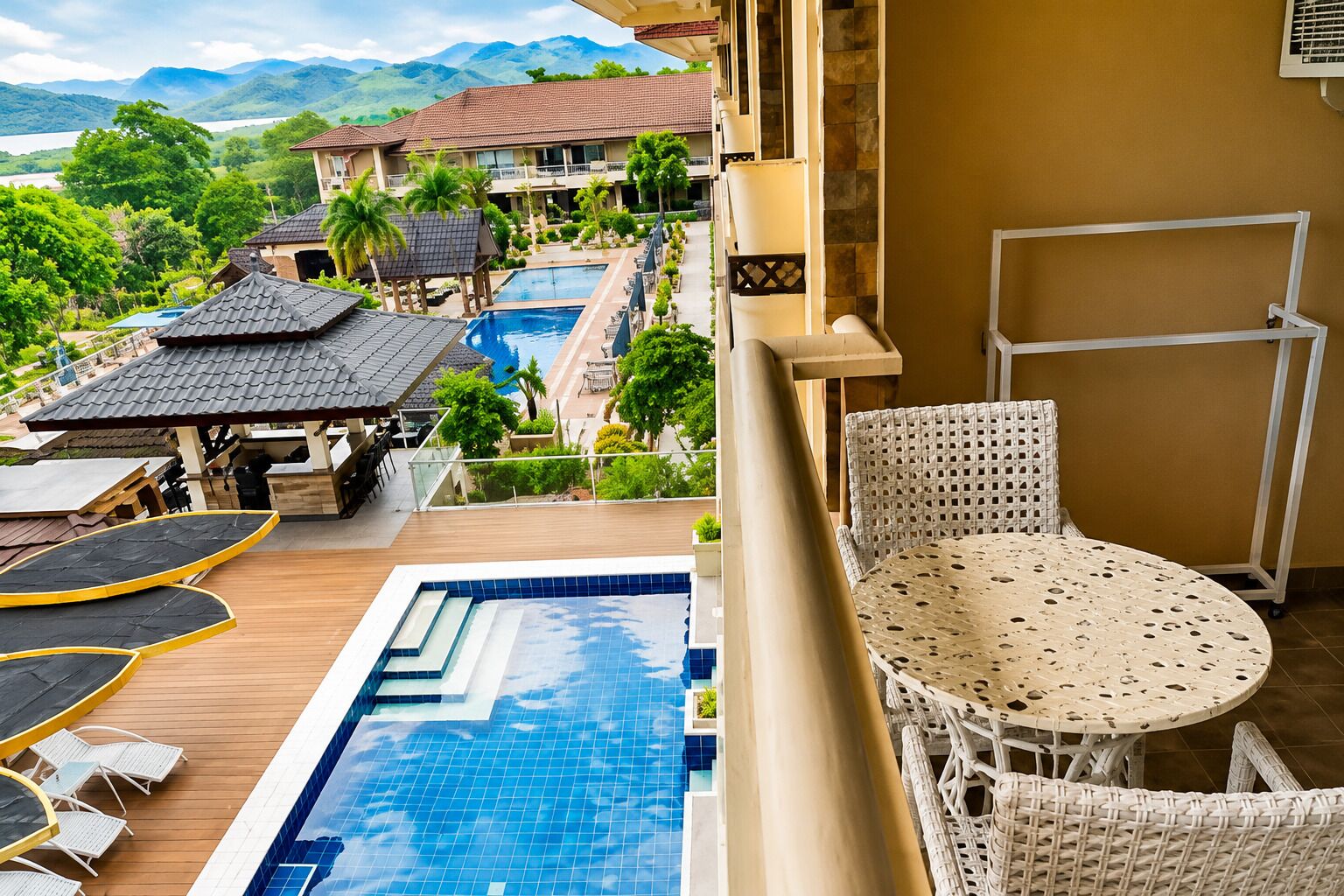 Un espace aménagé au bord de la piscine, offrant une vue sur un complexe hôtelier, comprenant une piscine, des chaises longues et une table.