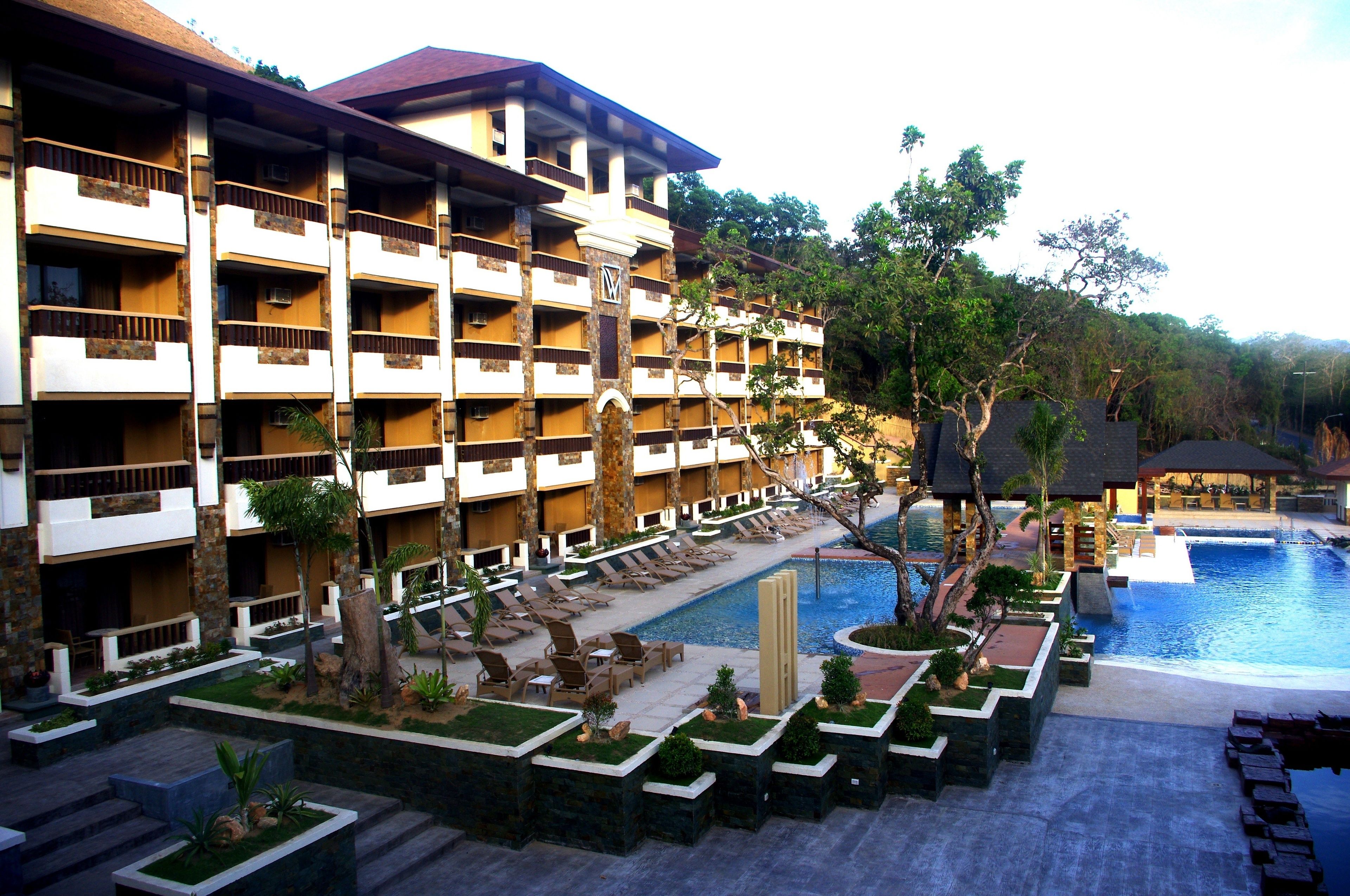 A multi-story hotel with balconies, a swimming pool, and landscaped gardens.