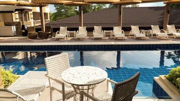 A pool area with lounge chairs and a table, surrounded by a building with a tiled roof and balconies.