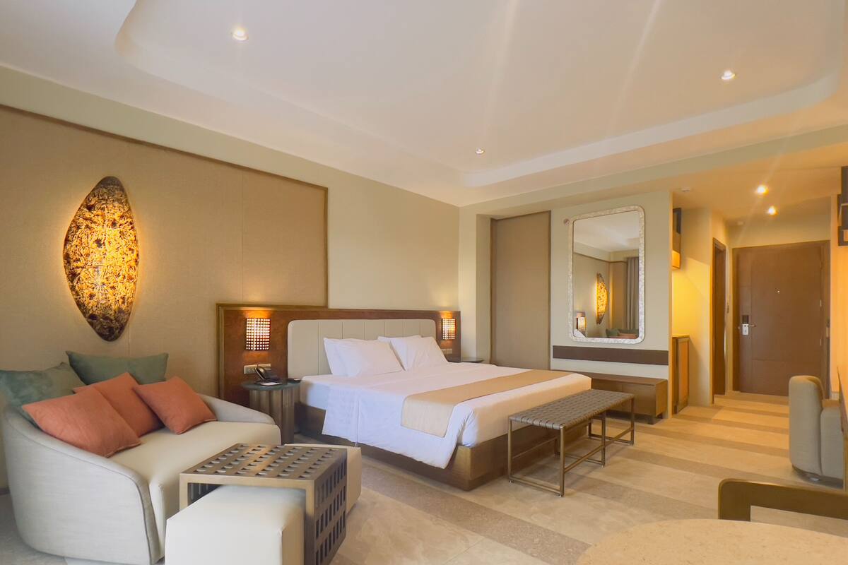 A modern hotel room with a large bed, a sofa, a small table, and a mirror.