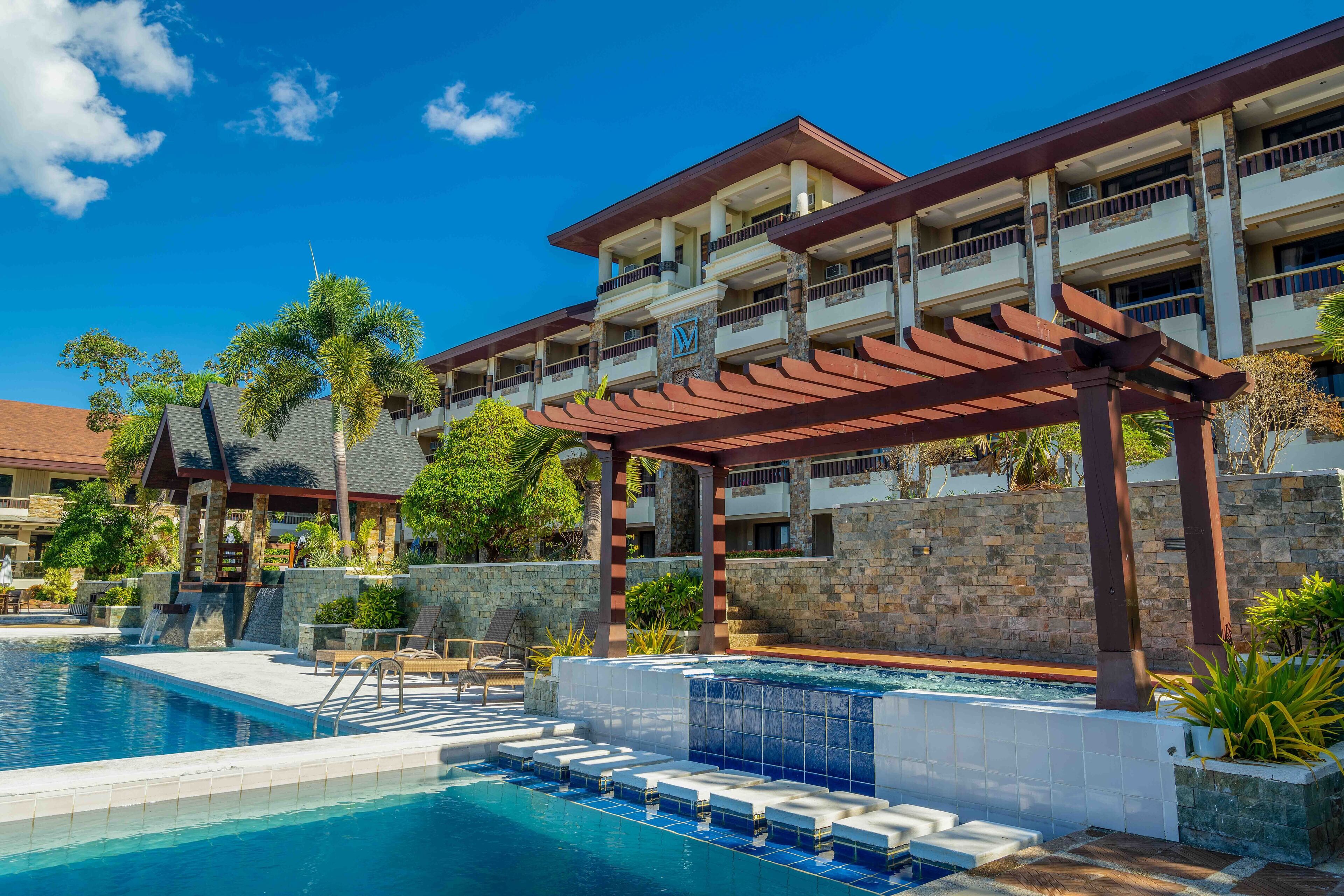 Un hotel con piscina, zona de estar exterior y un área cubierta con pérgola.
