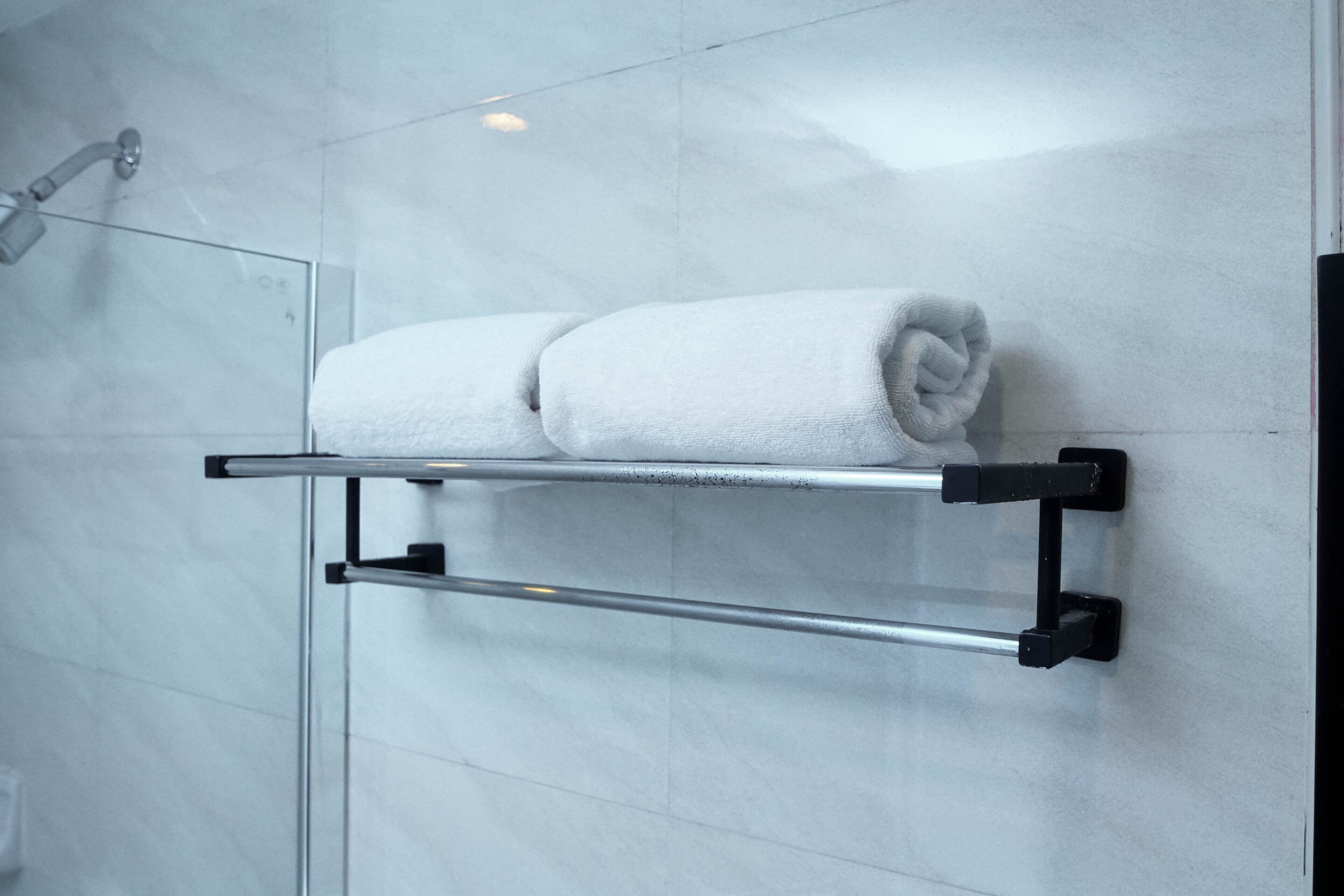 A bathroom with a glass shower enclosure, a towel rack with two white towels, and a metal towel bar.