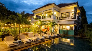 Une maison à deux étages avec une piscine, des chaises longues et un coin bar.