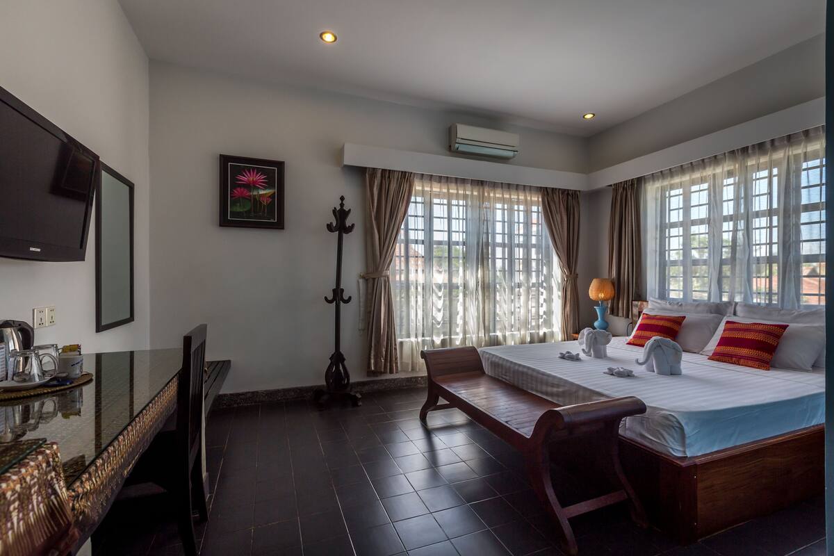 Habitación de hotel con cama, mesita de noche, lámpara y un ventanal grande con cortinas.