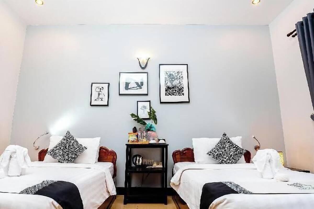 Habitación de hotel con dos camas, una mesita de noche y obras de arte en la pared.