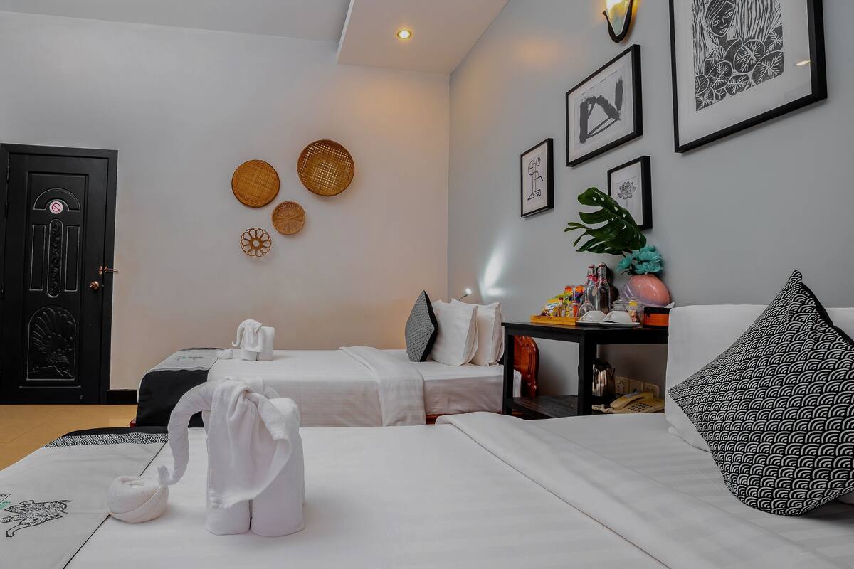 Habitación de hotel con dos camas, una puerta negra, cestas fijadas a la pared, obras de arte enmarcadas y una mesita con artículos de aseo.
