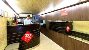 A hotel reception area with a wooden reception desk, a sofa, and a sign indicating under surveillance. - Acacia Inn (Jaipur)