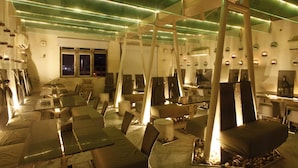 A modern dining area with glass tables and chairs, illuminated by green ceiling lights. - Acacia Inn (Jaipur)