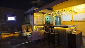 A modern outdoor bar area with seating and a counter, illuminated by string lights. - Acacia Inn (Jaipur)