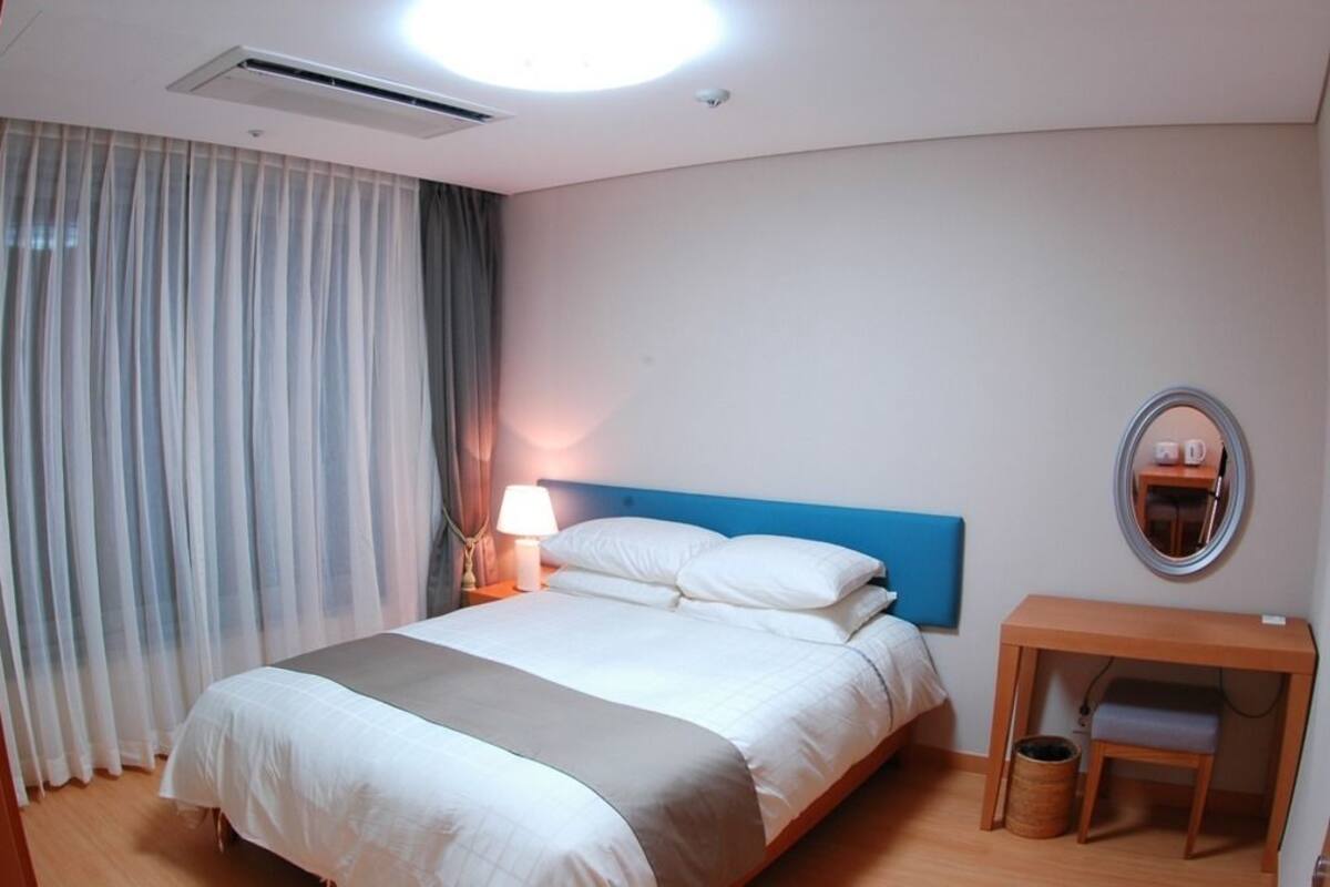 Une chambre d’hôtel avec un lit, une table de chevet avec une lampe, un miroir et un petit bureau en bois.