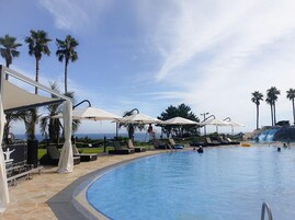A pool area with lounge chairs and umbrellas, palm trees, and a clear sky.