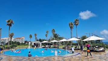 A pool area with palm trees, lounge chairs, and umbrellas.
