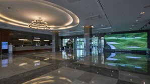 A spacious lobby with a modern chandelier, a reception desk, and a large screen displaying a golf course. - Kumho Jeju Resort (Seogwipo)