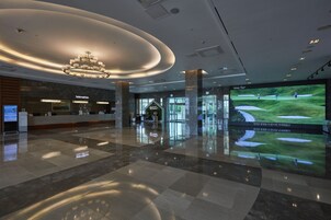 A spacious lobby with a modern chandelier, a reception desk, and a large screen displaying a golf course.
