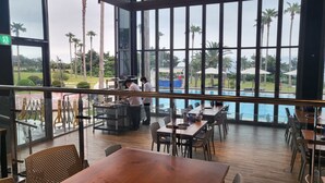 A restaurant with large windows overlooking a pool and palm trees. - Kumho Jeju Resort (Seogwipo)