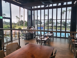 A restaurant with large windows overlooking a pool and palm trees.