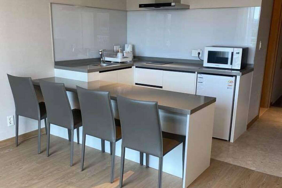 Une cuisine moderne avec un îlot central, quatre chaises grises et un four à micro-ondes.