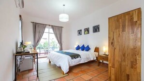 Un dormitorio con cama, escritorio, silla, armario de madera y ventana con cortinas.