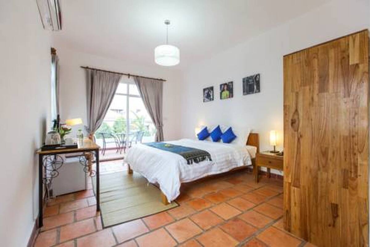 Een slaapkamer met een bed, een bureau, een stoel, een houten garderobe en een raam met gordijnen.
