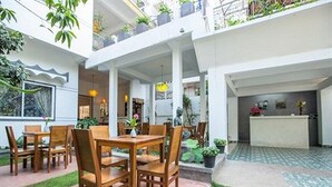 Un patio interior espacioso con zona de comedor, mostrador de recepción y plantas en macetas.