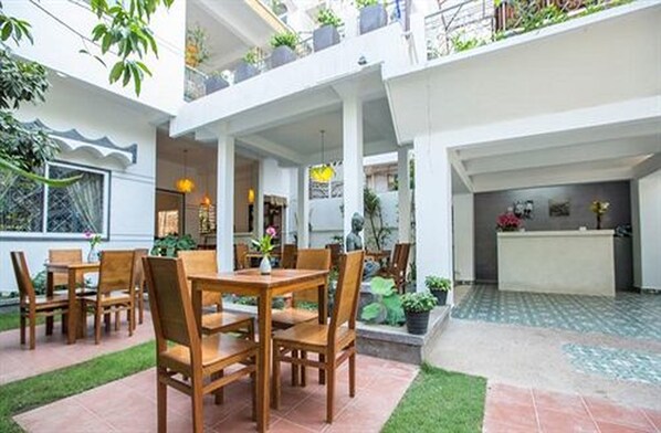 A spacious indoor courtyard with a dining area, a reception desk, and potted plants.