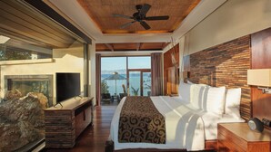 Un dormitorio amplio con una cama grande, un ventilador de techo, una chimenea de piedra y vistas al mar.
