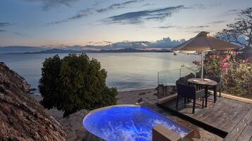 A hot tub with a view of the sea, a wooden deck, and a table with an umbrella.